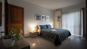 A modern bedroom with a bed, bedside tables, a potted plant, and a large window with curtains.
