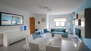 A modern living room with a light blue sofa, a white dining table with chairs, and a large mirror on the wall.