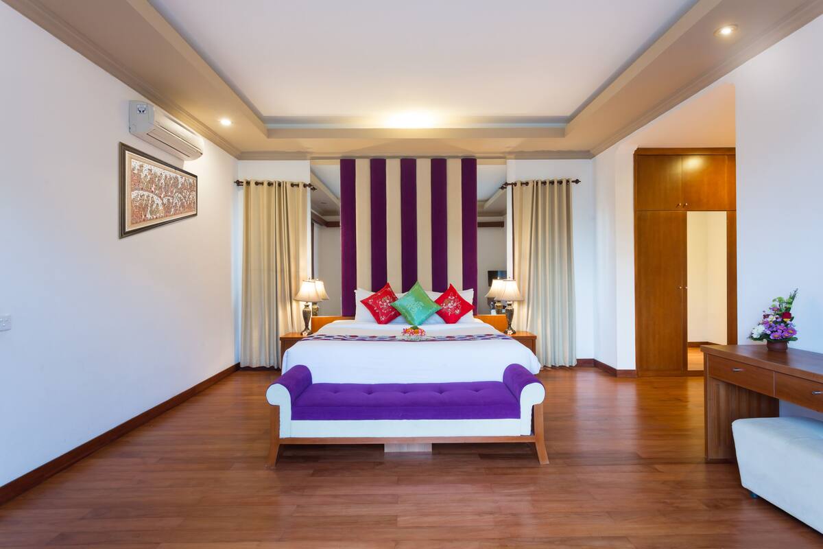 A hotel room with a large bed, a wooden desk, and a bench.