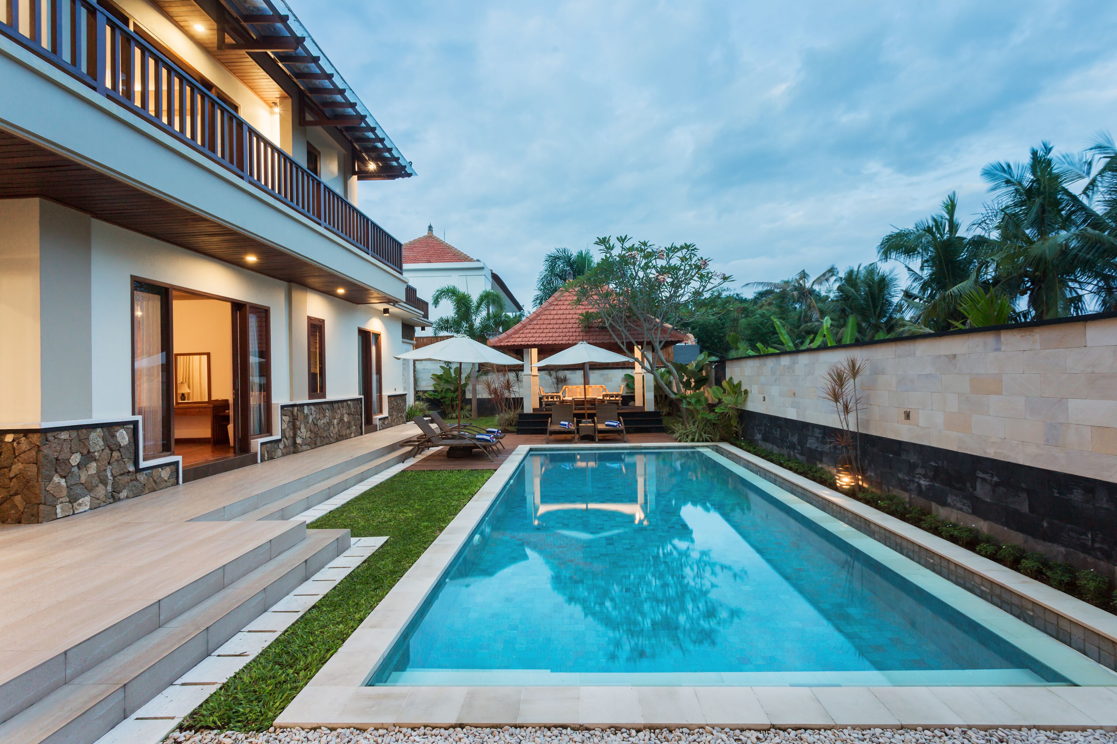 Una casa moderna con piscina, un patio cubierto y un muro de piedra.