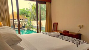 A hotel room with a large bed, a small desk, a chair, and a view of an outdoor swimming pool. - Villa Sabasanti (Blahbatuh)