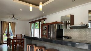 A modern kitchen with a bar area, wooden stools, and a dining table with chairs. - Villa Sabasanti (Blahbatuh)