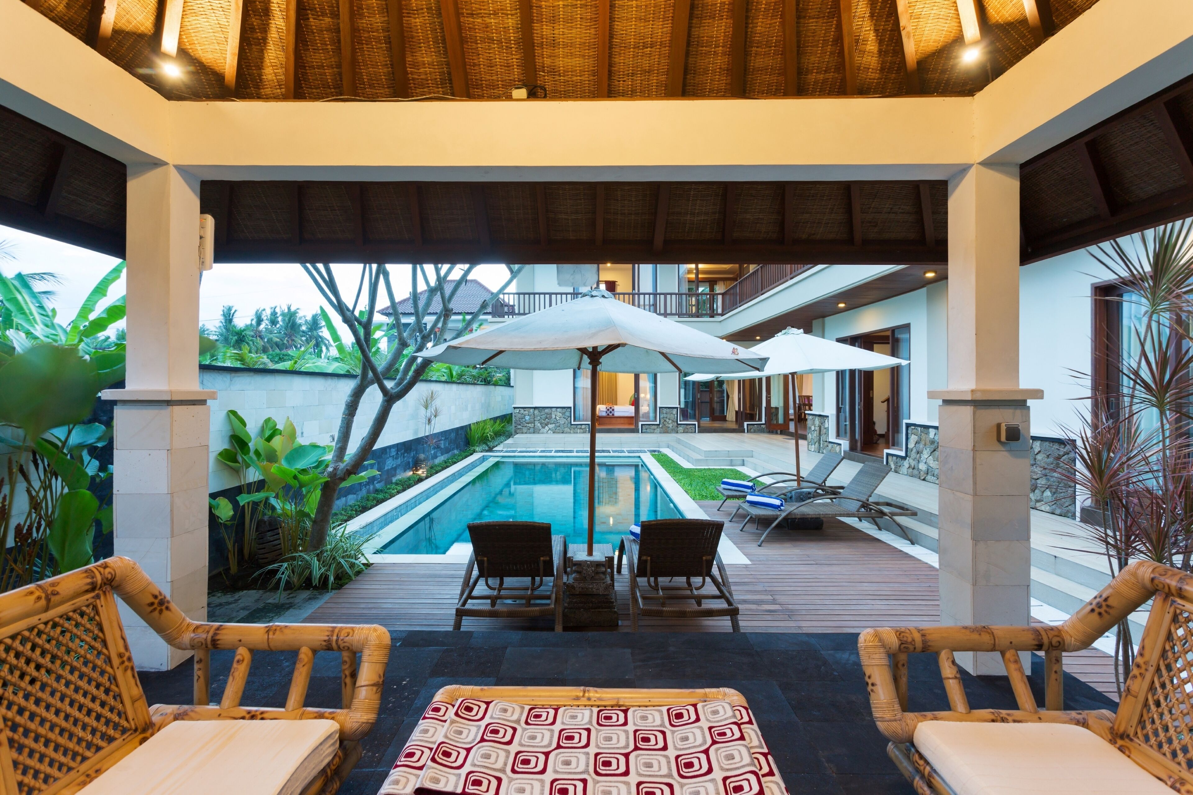 A covered outdoor area with a pool, lounge chairs, and umbrellas.