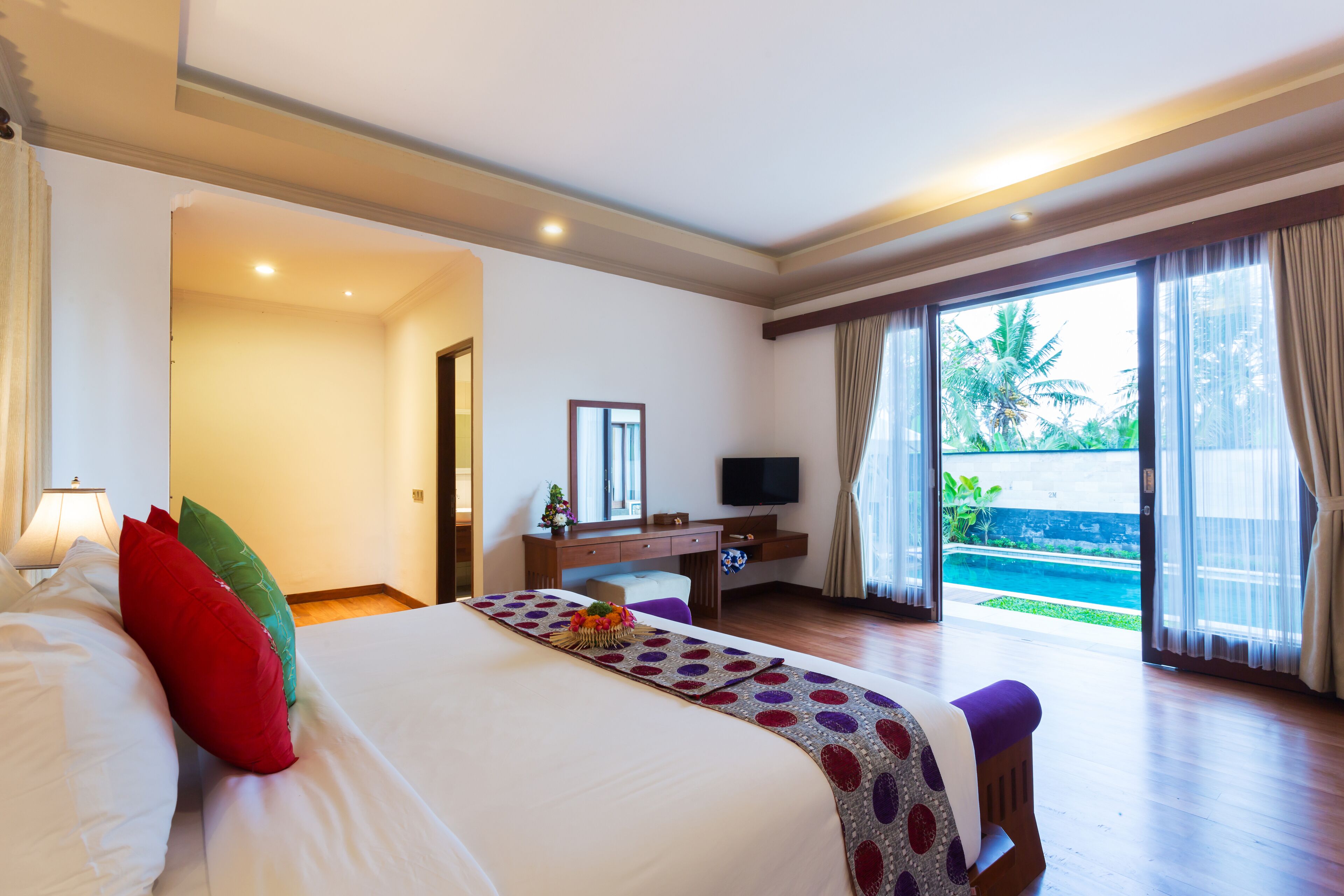 A hotel room with a bed, a desk, a television, and a view of a swimming pool.