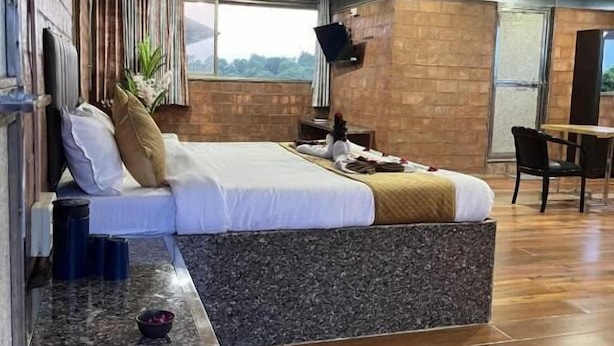 A modern bedroom with a bed, a small table, a chair, and a TV mounted on the wall. - Shri Shiv Villa Managed By Blue Diamond (Mendarda)