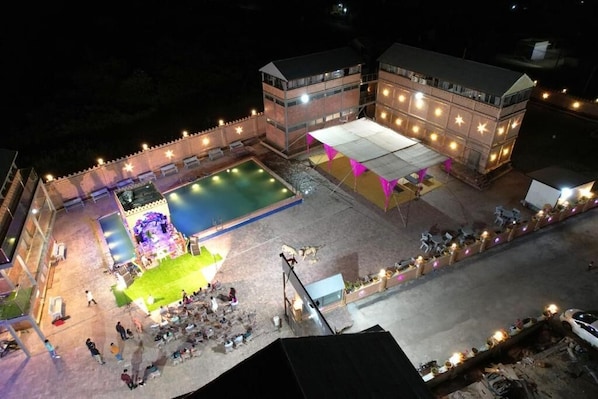 A hotel with a swimming pool, outdoor seating, and a stage for events. - Shri Shiv Villa Managed By Blue Diamond (Mendarda)