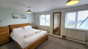 Une chambre à coucher avec un lit en bois, des tables de chevet, un miroir et des fenêtres équipées de stores.