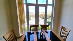 A dining area with a table and four chairs, a window with a view of a landscape, and a curtain partially drawn.