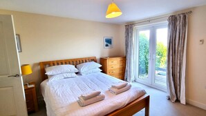 A bedroom with a bed, bedside table, lamp, and a view of the outdoors through a window.