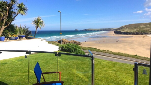 A view of a beach from a covered area with a chair and a railing. - Luxury, 3 bedroom apartment with stunning sea views! (Perranporth)