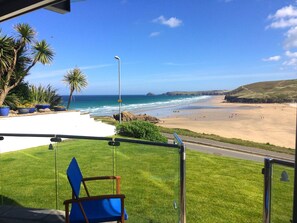 A view of a beach from a covered area with a chair and a railing. - Luxury, 3 bedroom apartment with stunning sea views! (Perranporth)