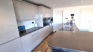 A modern kitchen with white cabinets, a large island, and built-in appliances. - Luxury, 3 bedroom apartment with stunning sea views! (Perranporth)
