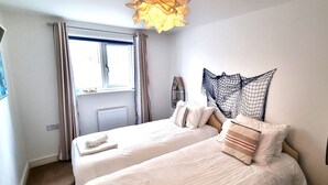 A bedroom with two beds, a window with curtains, a wall-mounted shelf, and a unique spider web design on the wall. - Luxury, 3 bedroom apartment with stunning sea views! (Perranporth)