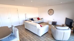 A modern living room with a sofa set, a television, and a clock on the wall. - Luxury, 3 bedroom apartment with stunning sea views! (Perranporth)
