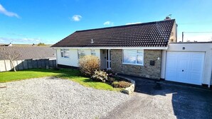 A two-story house with a stone facade, a tiled roof, and a white garage door. - Spacious holiday home with wrap around gardens (Perranporth)