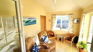 A cozy room with wicker furniture, a wooden door, and a window with curtains. - Spacious holiday home with wrap around gardens (Perranporth)