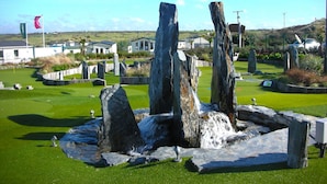 A golf course with a rocky centerpiece, surrounded by well-maintained grass and stone structures. - Chalet on Perran Sands, Haven holiday park (Perranporth)