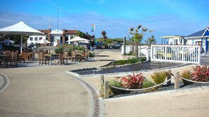 An outdoor seating area with tables and chairs, a reception tent, and a fenced garden area with plants. - Chalet on Perran Sands, Haven holiday park (Perranporth)