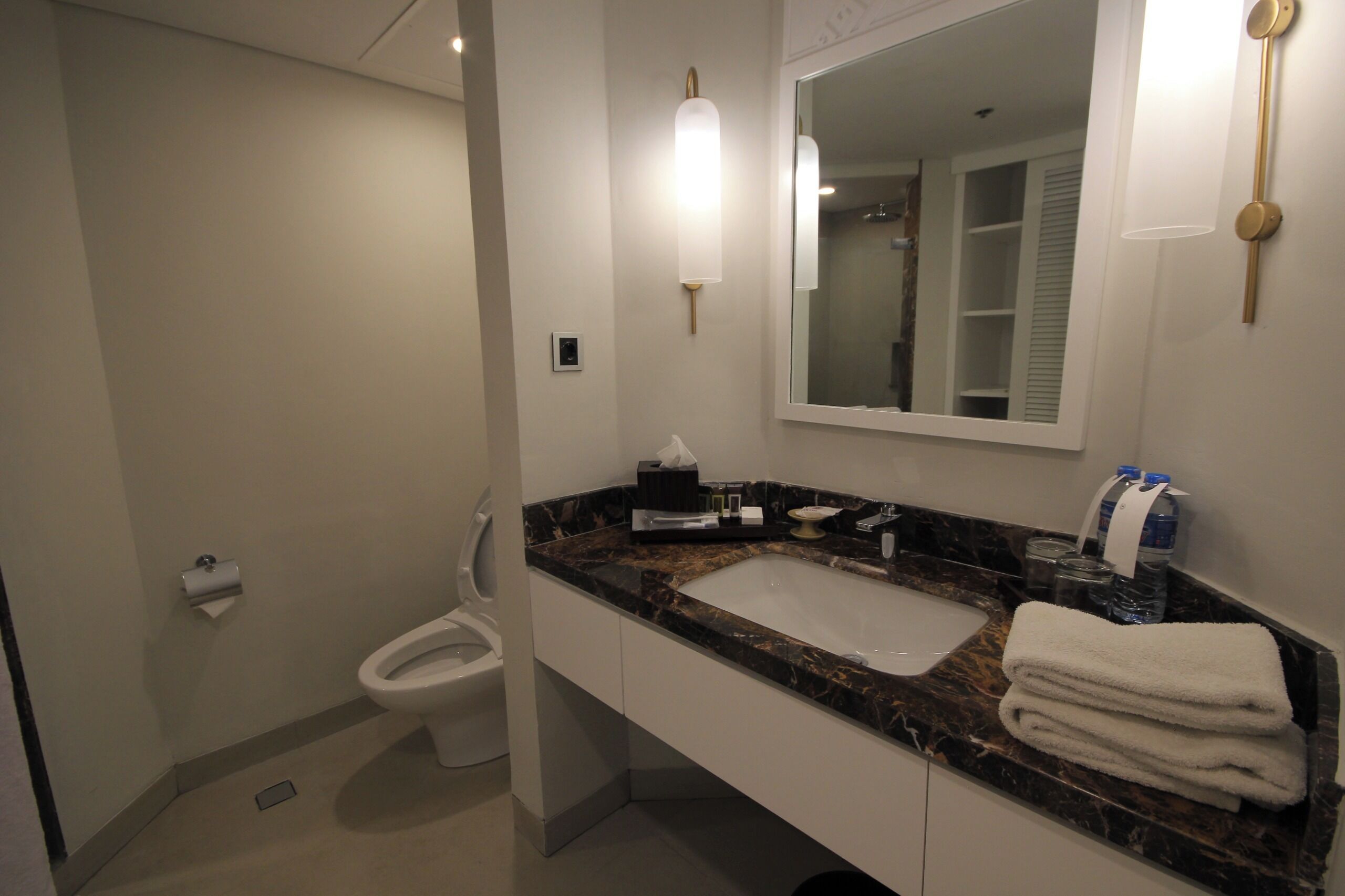 A bathroom with a marble sink, a toilet, a mirror, and a towel rack.