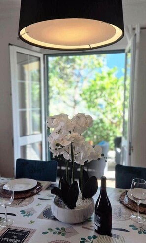 A dining table with a white floral centerpiece, wine bottles, and glasses, set in a room with a view of greenery outside. - Casa Brisa - by PrimeStayMadeira (São Vicente)