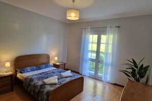 Een slaapkamer met een bed, nachtlampjes, een raam met gordijnen en een plant in pot.