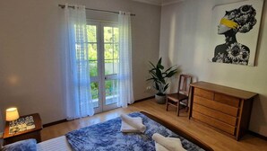 A bedroom with a bed, a dresser, a chair, a lamp, and a window with curtains. - Casa Brisa - by PrimeStayMadeira (São Vicente)