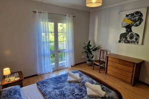 A bedroom with a bed, a dresser, a chair, a lamp, and a window with curtains. - Casa Brisa - by PrimeStayMadeira (São Vicente)