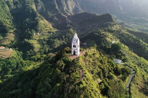 A white church with a clock tower on a hillside surrounded by lush greenery. - Casa Brisa - by PrimeStayMadeira (São Vicente)