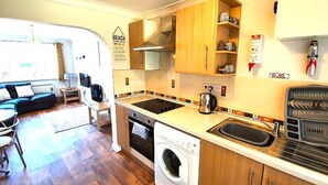 A compact kitchen with wooden cabinets, a washing machine, a kettle, and a sink. - Beachfront apartment with direct beach access! (Perranporth)