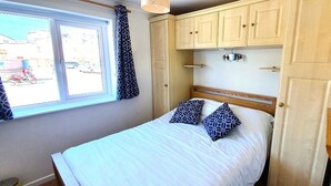 A bedroom with a bed, a window with curtains, and a wooden wardrobe. - Beachfront apartment with direct beach access! (Perranporth)