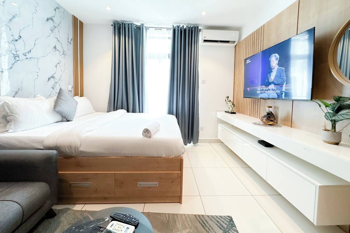 Una habitación de hotel moderna con una cama, un televisor, una consola de madera y una planta en maceta.