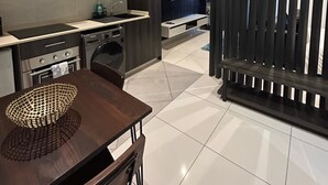 A modern kitchen with a dining area, featuring stainless steel appliances, a flat-screen TV, and a decorative wall panel. - Embassy Gardens Haven (Accra)