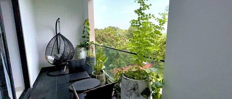A balcony with a table and chairs, potted plants, and a hanging chair.