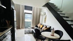 A modern living room with a dining area, a kitchen with a washing machine, and a staircase. - Embassy Gardens Haven (Accra)
