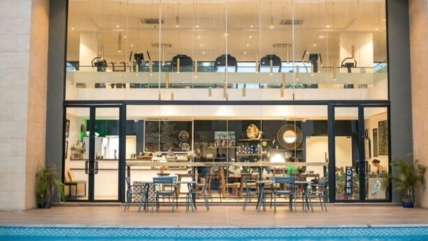 A modern restaurant with a glass facade, outdoor seating, and a pool area. - Embassy Gardens Haven (Accra)