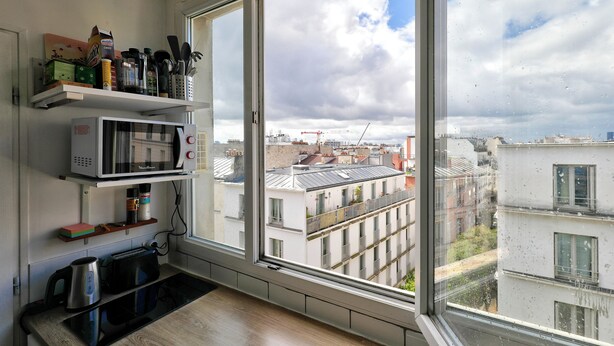 A kitchen with a large window, a microwave, and various kitchen items on shelves. - Studio overlooking the rooftops of Paris, 2 minutes from the metro (Paris)
