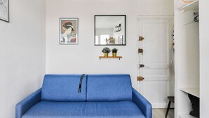 A room with a blue sofa, a white door, a mirror, and a framed picture on the wall. - Studio overlooking the rooftops of Paris, 2 minutes from the metro (Paris)