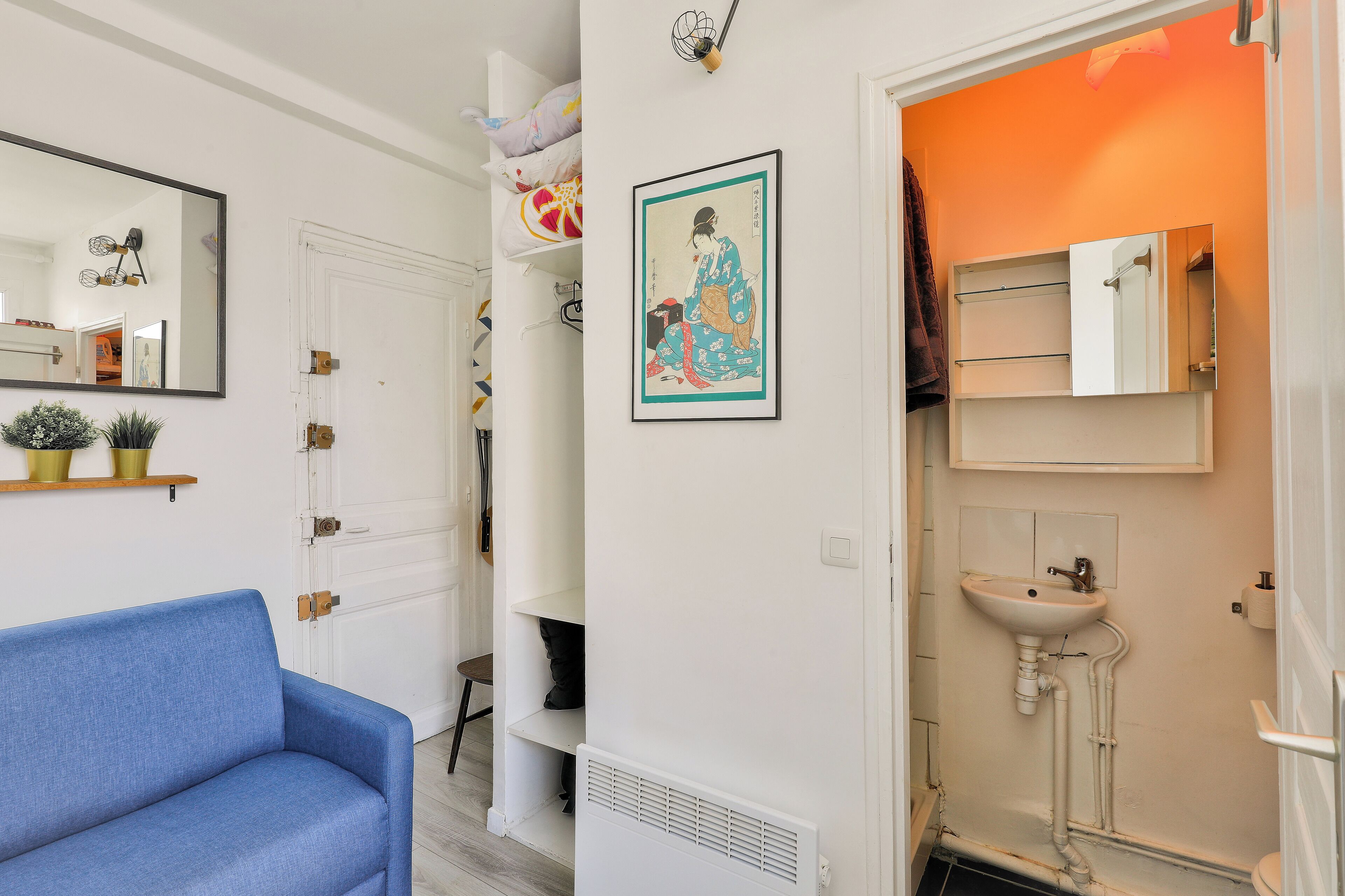 A room with a blue sofa, a white door, a framed artwork, a white sink, and an orange wall.