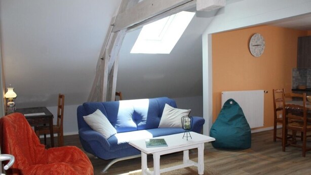 A cozy loft-style room with a sloped ceiling, a blue sofa, a white coffee table, and a green bean bag.