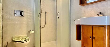 A bathroom with a glass-enclosed shower, a toilet with a green seat, and wooden cabinets.