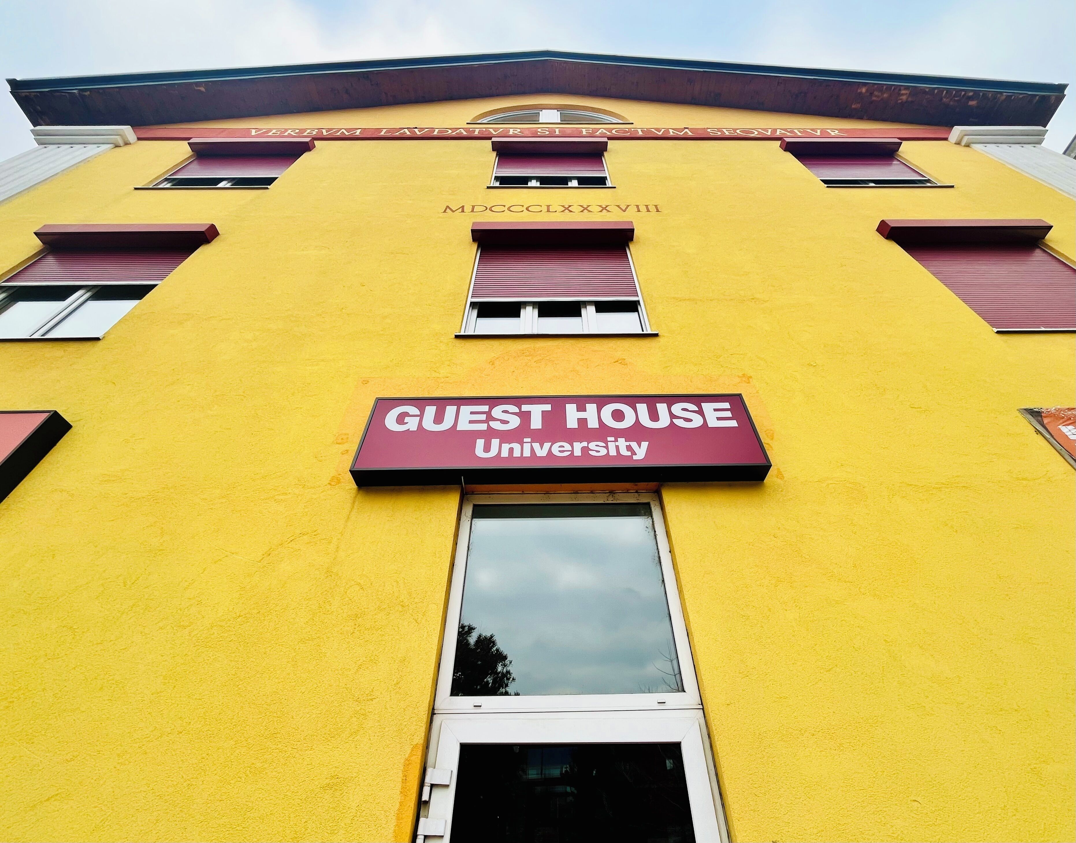 Ein gelbes Gebäude mit einem scharlachroten Schild, auf dem „GUEST HOUSE University“ und die Registrierungsnummer „MDCCCLXXXVIII“ steht.