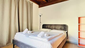 A neatly made bed with white linens and towels, a grey upholstered headboard, and a wooden floor.