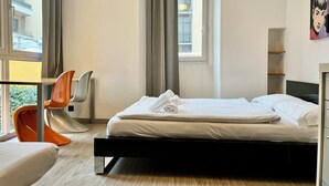 A hotel room with a bed, a desk, an orange chair, and a window with curtains. - GuestHouse Lugano University (Lugano)