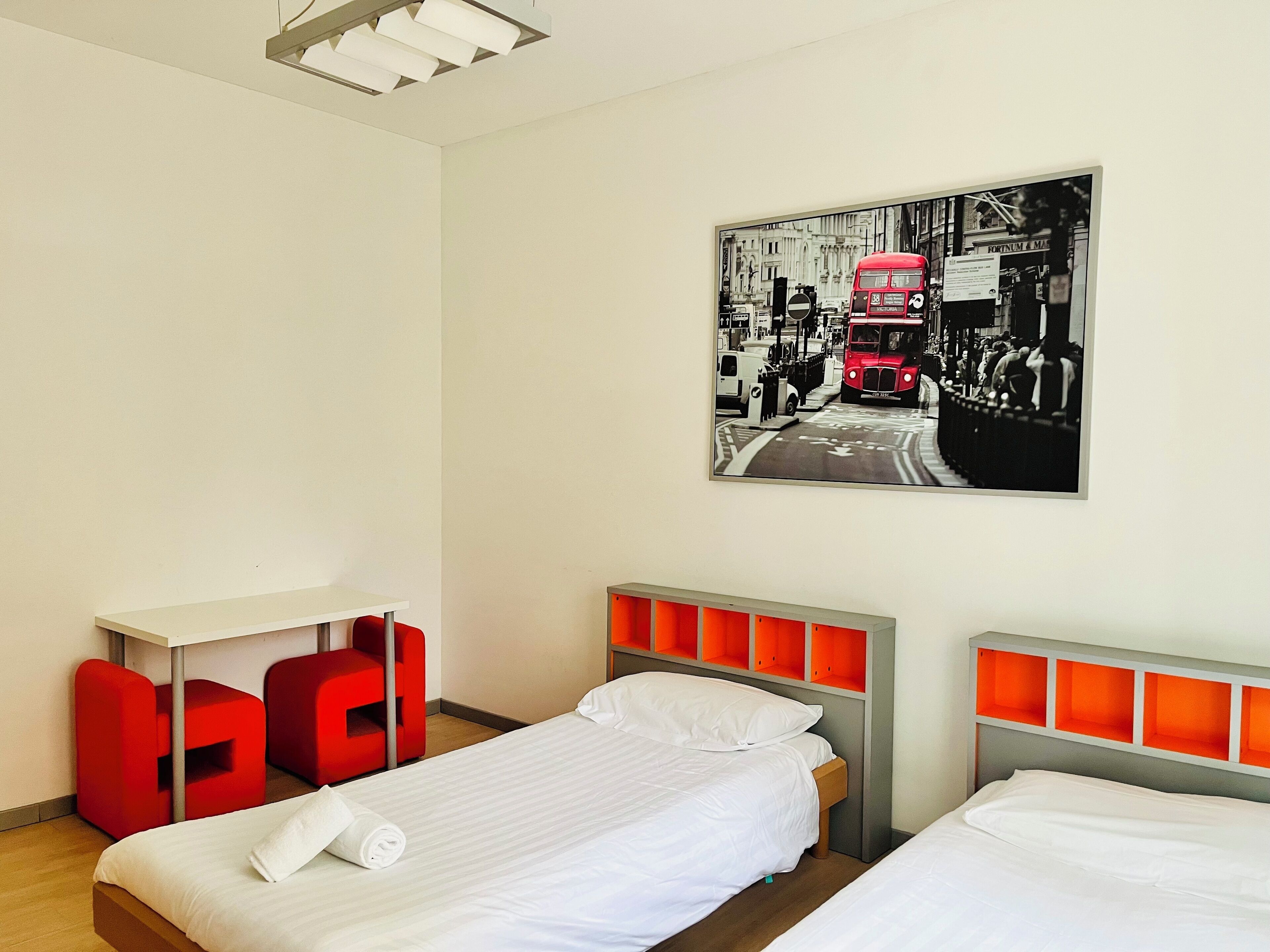 Ein Hotelzimmer mit zwei Betten, einem Schreibtisch und roten Stühlen.