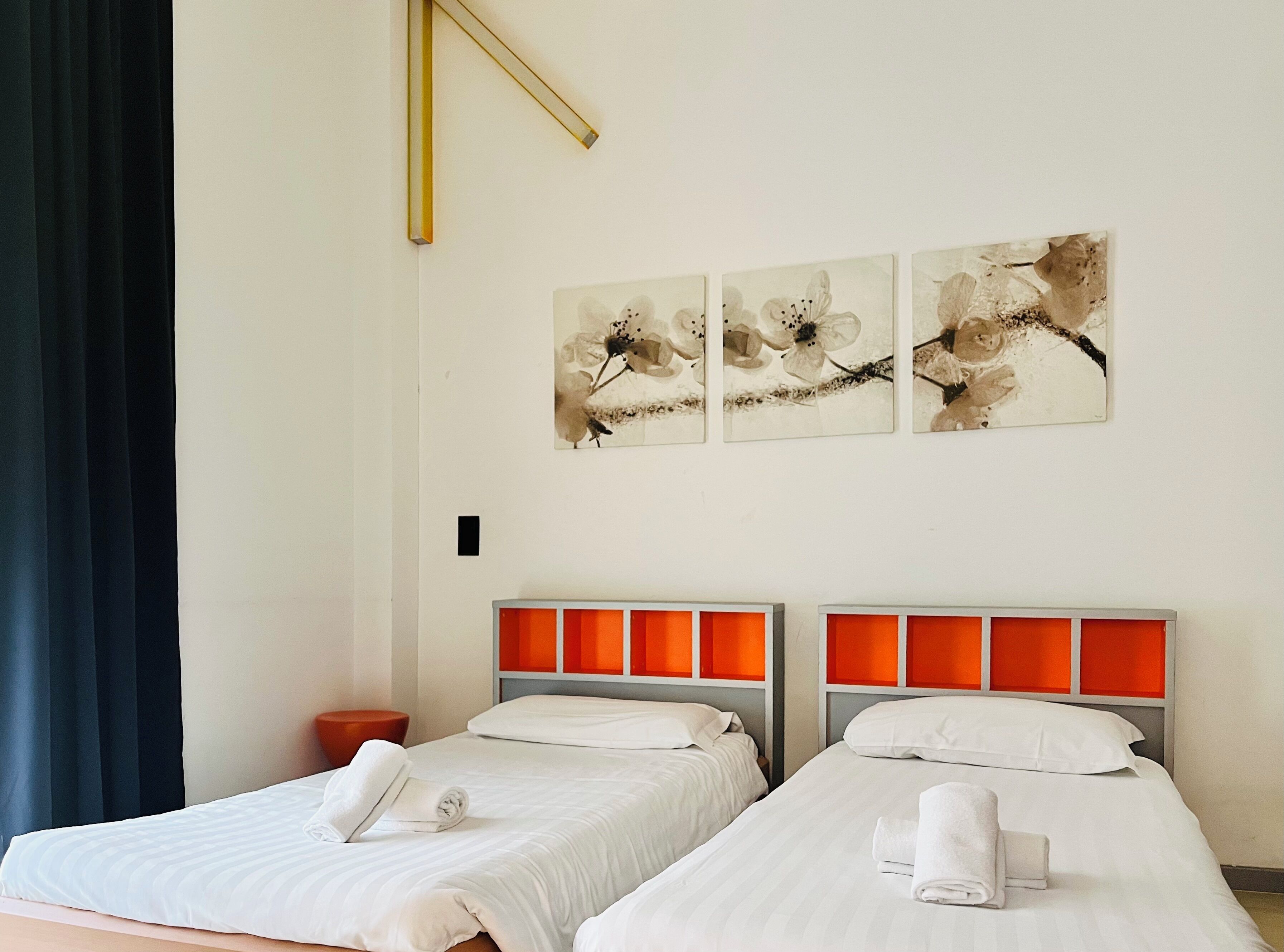 Habitación de hotel con dos camas, ropa blanca y un ventanal grande con cortinas oscuras.