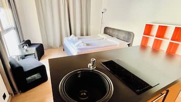 A modern hotel room with a bed, a desk, a chair, a black sink, and a small table.