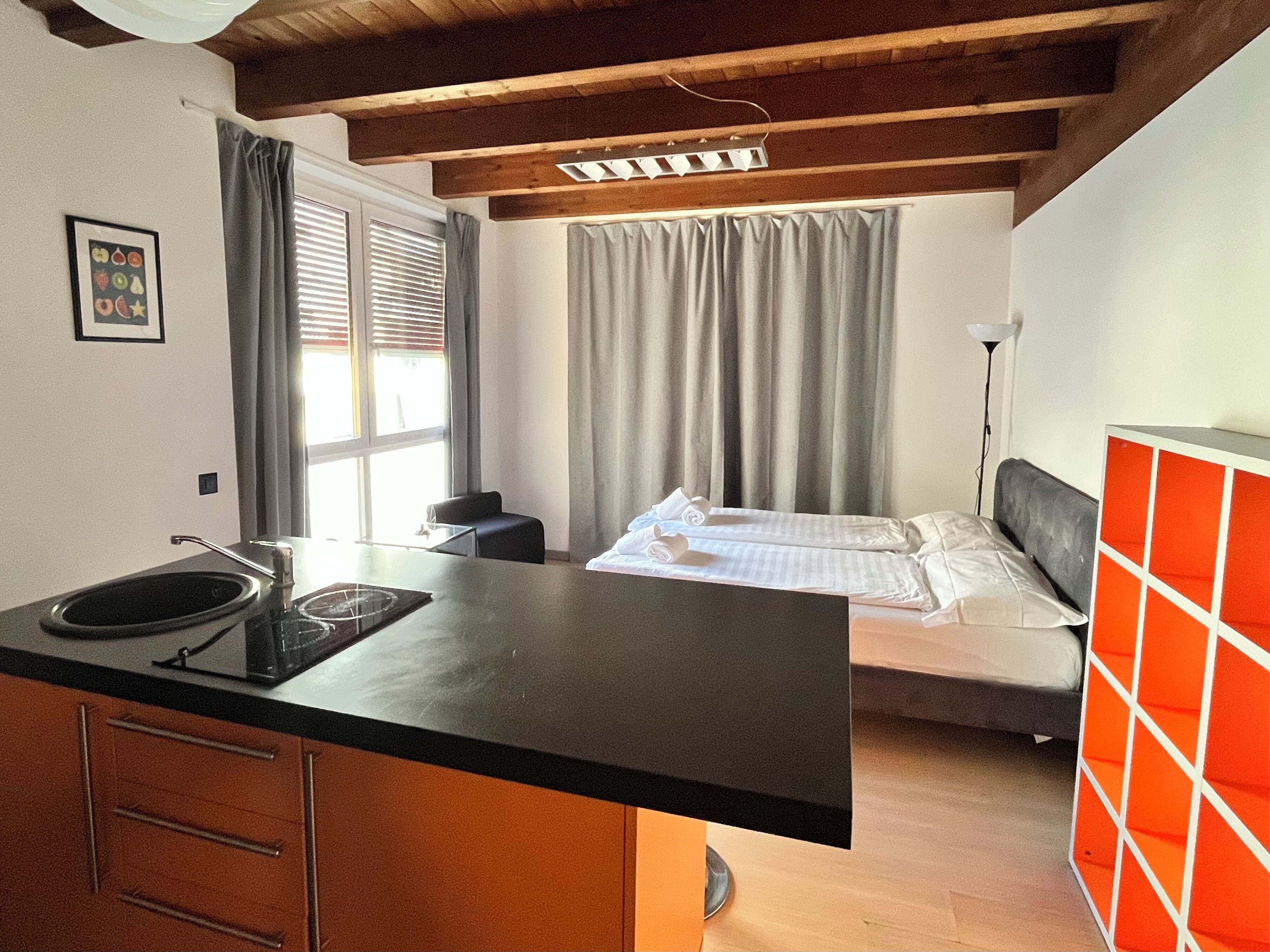 A compact hotel room with a kitchenette, a bed, and a window with curtains.