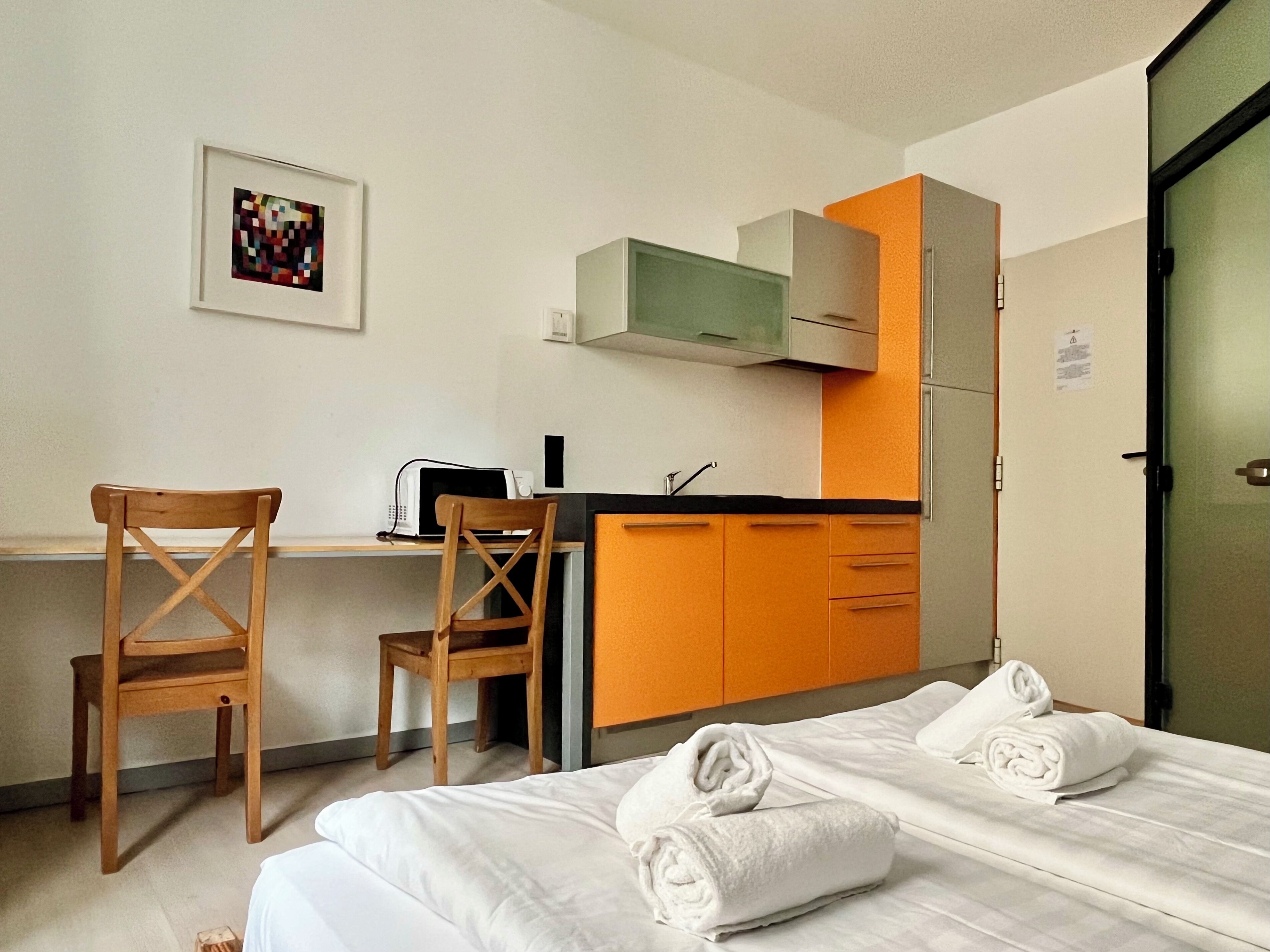 Habitación de hotel con cama, escritorio con microondas, una silla y kitchenette.