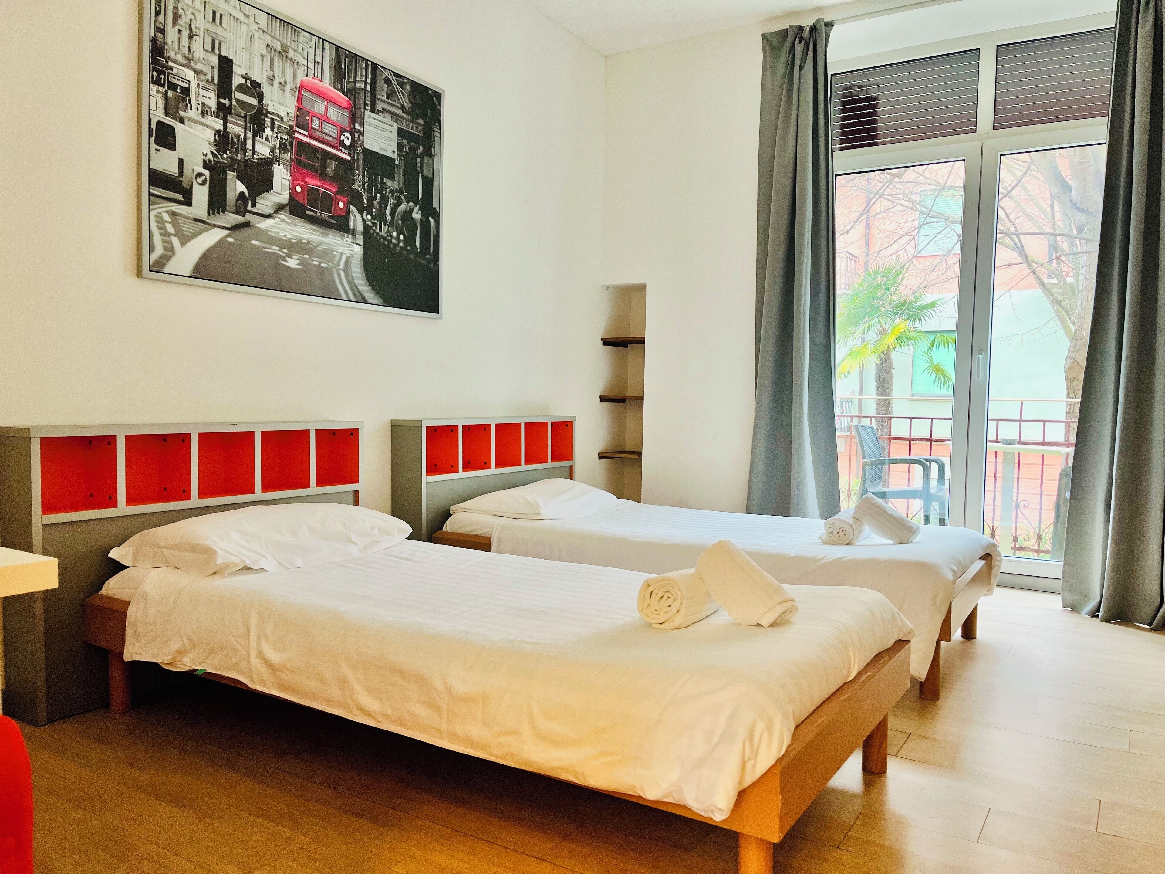 Habitación de hotel con dos camas, un ventanal con vistas y un cuadro de un autobús rojo de dos pisos.