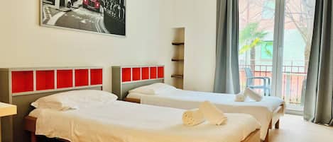 Habitación de hotel con dos camas, un ventanal con vistas y un cuadro de un autobús rojo de dos pisos.